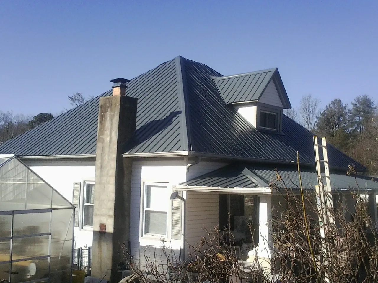 Dark blue standing seam metal roof on a white farmhouse with dormer — Slate & Tile Roof Repair by Roofing Brothers in Volin