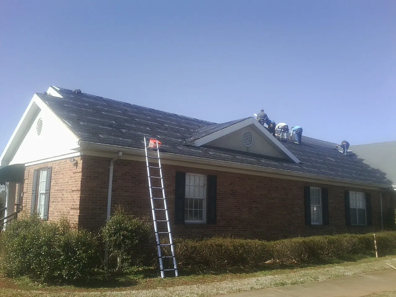 Crew tearing shingles off a brick ranch roof with a ladder set — Emergency Roof Repair work by our crew in Volin