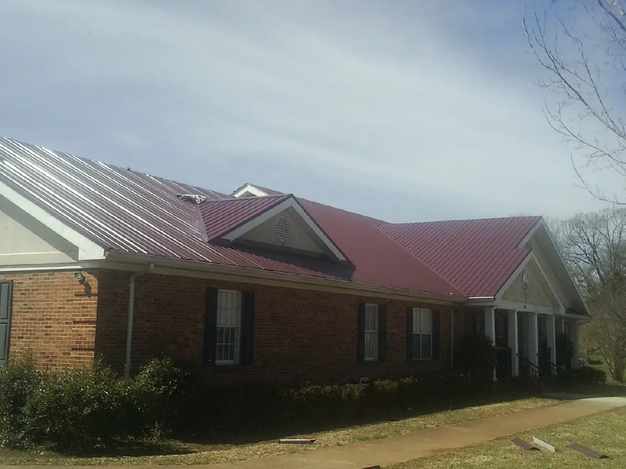 Red metal roof with gabled entries on a long brick building, from a Hail Damage Roof Repair job in Volin