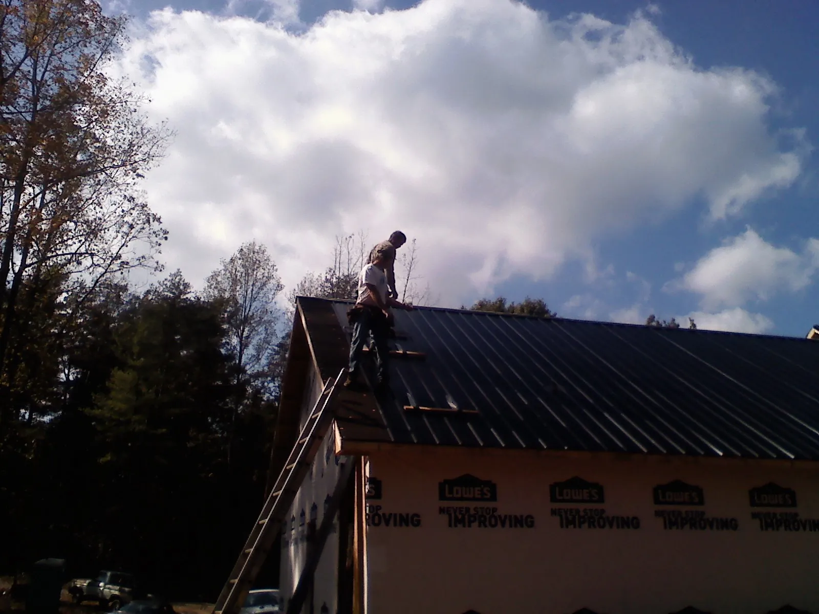 Roofer fastening dark metal panels high against a cloudy sky, from a Roof Inspection job in Volin